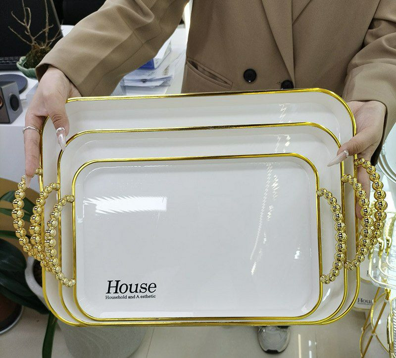 Ensemble de trois plateaux de service blancs et noires de différentes tailles, avec des bords dorés et des poignées dorées en forme de perles et autres.